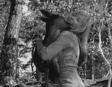 a black and white photo of a woman holding a deer in her arms .