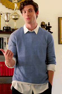 a young man wearing a blue sweater and a white shirt is standing in front of trophies on a shelf