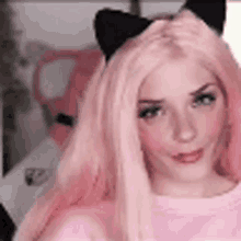 a woman with pink hair and black cat ears is wearing a pink shirt .