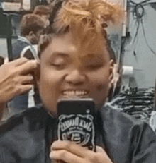 a man is getting his hair cut by a barber while holding a jack daniels can .