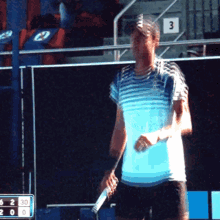 a man in a blue and white striped shirt is holding a tennis racquet in front of a scoreboard with the number 3 on it