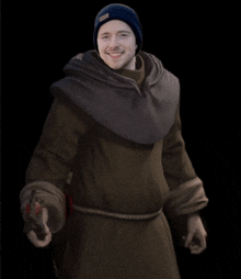 a man wearing a hooded robe and a beanie is smiling and holding a gun