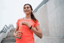 a woman in an orange shirt is holding an orange bottle of water