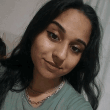 a woman wearing a green shirt and a silver chain around her neck looks at the camera