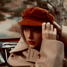 a woman wearing a red hat and a tan coat has a ring on her finger