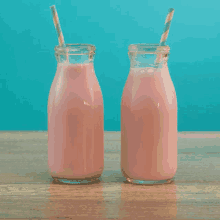 two milk bottles filled with pink liquid and straws