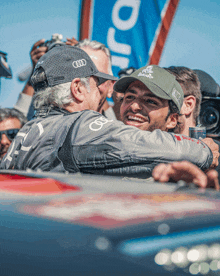 a man wearing an audi hat is hugging another man in a crowd