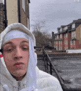 a young man wearing a white hooded jacket and a white headband stands in front of a row of houses