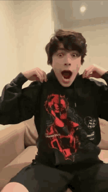 a young man is sitting on a couch wearing a black hoodie with a picture of a skull on it