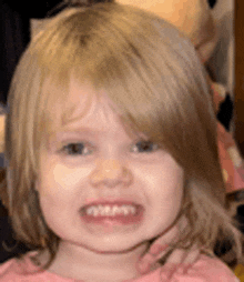 a little girl with blonde hair and a pink shirt is crying and making a funny face .