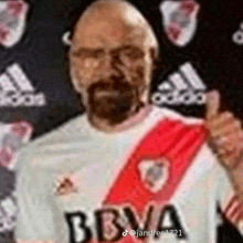 a bald man with a beard is wearing a bbva shirt and giving a thumbs up .