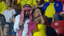 a man in a sheikh costume is holding a flag next to a woman in a yellow jersey .