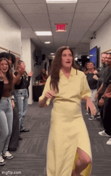 a woman in a yellow dress is dancing in a hallway surrounded by people .