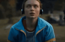 a woman in a blue jacket is wearing headphones and looking up .