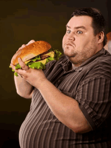 a man in a striped shirt is holding a large hamburger