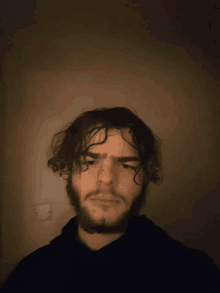 a man with curly hair and a beard looks at the camera in a dark room