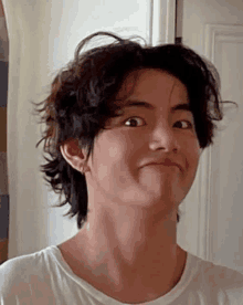 a young man with curly hair is making a funny face while wearing a white t-shirt .