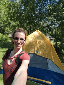 a woman taking a selfie in front of a yellow and blue tent that says mountaineer