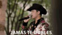 a man in a cowboy hat is singing into a microphone with the words " jamas te dobles " above him