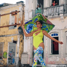 a woman in a yellow bodysuit and floral pants is standing in front of a building with graffiti on it