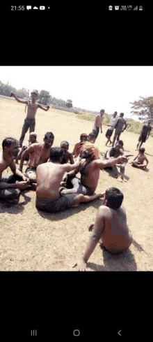 a group of shirtless men are sitting in a circle on a grassy field