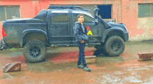 a man is standing in front of a black truck with a snorkel on the roof .