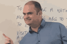 a man in a blue shirt is pointing at something on a whiteboard .