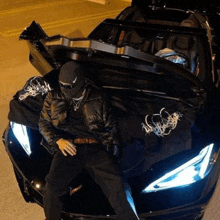 a man is sitting in the trunk of a black sports car with the hood open .