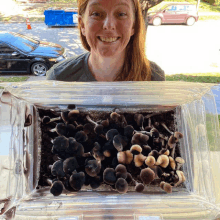 a woman is smiling while holding a plastic container of mushrooms