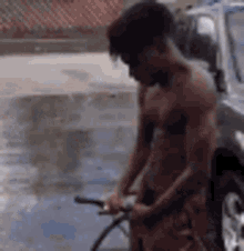 a shirtless man is washing a bicycle in the rain .