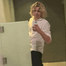 a man in a white shirt is taking a selfie in a bathroom stall