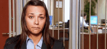 a woman in a suit and blue shirt is standing in front of a window in an office behind bars .