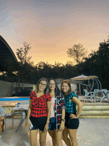 three women are posing for a picture in front of a swimming pool