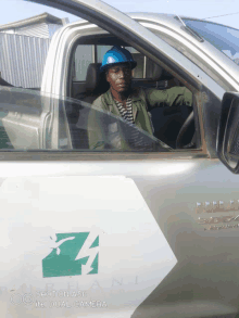 a man wearing a blue hard hat is sitting in the driver 's seat of a car with the letter h on the side