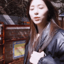 a woman in a black leather jacket stands in front of a brick wall with a sign that says ' a ' on it