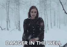 a woman in a black dress stands in a snowy forest with the words danger in the well below her