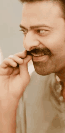 a man with a mustache is smiling and touching his face with his hand .