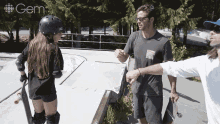 a girl wearing a helmet and knee pads talks to a man holding a skateboard in front of a gem ad