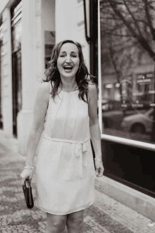 a woman in a white dress is laughing while holding a clutch