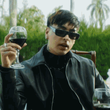 a man wearing sunglasses and a leather jacket is holding a glass of wine