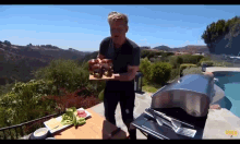 a man is standing in front of a grill holding a tray of food with a gma logo in the corner