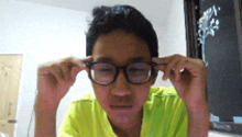 a boy wearing glasses and a yellow shirt looks at the camera