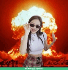 a woman wearing sunglasses is standing in front of a huge explosion .