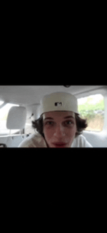 a young man wearing a white hat with the letter m on it is sitting in the back seat of a car .