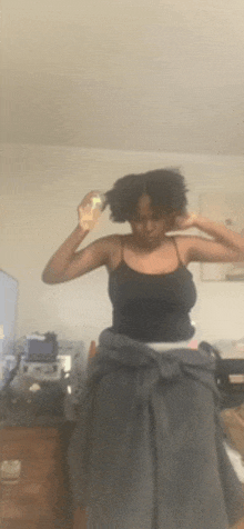 a woman is brushing her hair in a room while wearing a black tank top .