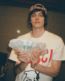 a man wearing a gucci shirt is holding a bunch of money in his hands