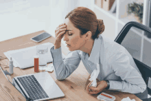 a woman is sitting at a desk with a laptop and a box of pills