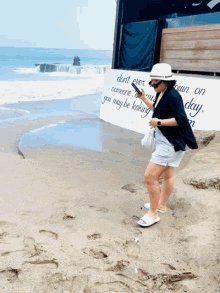 a woman stands on a beach near a sign that says " do n't ever someone you may be looking "