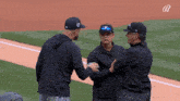 three men are standing on a baseball field and one of them is wearing a hat with the letter b on it