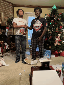 two men are shaking hands in front of a christmas tree and one has an american shirt on